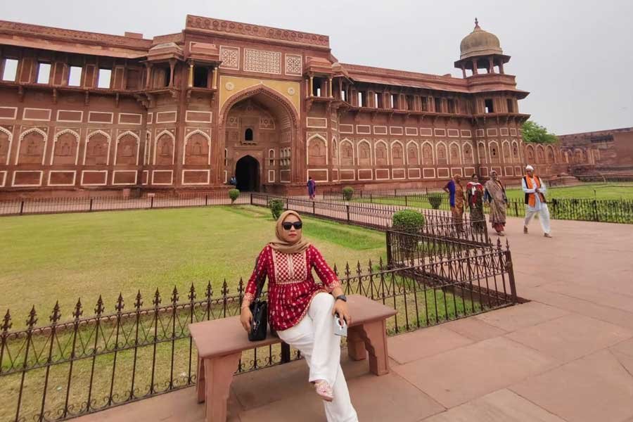 A girl sitting in front of the historic Agra Fort, surrounded by beautiful Mughal architecture and gardens.