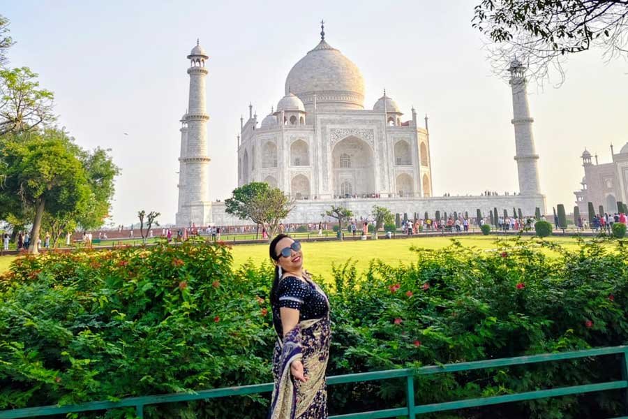 A woman posing in saree in front of the iconic Taj Mahal, surrounded by lush green gardens in Agra.