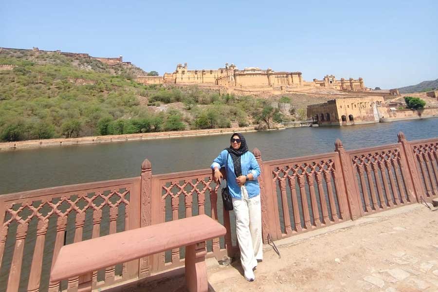 A woman posing near the scenic Amer Fort in Jaipur, with beautiful lake views and historic architecture in the background.