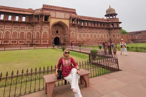 A girl sitting in front of the historic Agra Fort, surrounded by beautiful Mughal architecture and gardens.