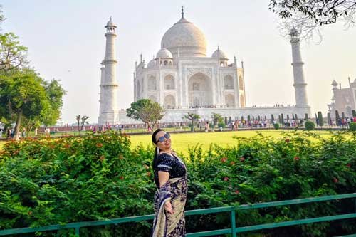 A woman posing in saree in front of the iconic Taj Mahal, surrounded by lush green gardens in Agra.