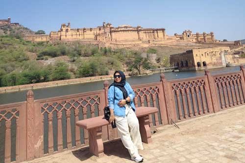 A woman posing near the scenic Amer Fort in Jaipur, with beautiful lake views and historic architecture in the background.